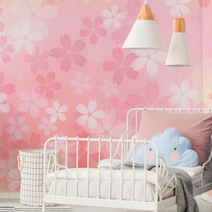 May include: A white metal bed with a pink pillow and a blue cloud-shaped pillow. The background features a pink floral wallpaper. Two white pendant lights hang above the bed. A black arrow with white dots sits on a striped rug.