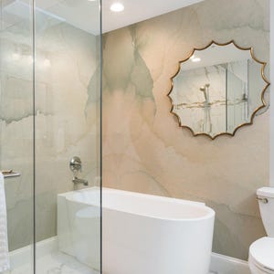 May include: A modern bathroom featuring a white, oval-shaped bathtub, a glass shower enclosure, and a decorative mirror with a gold frame. The walls have a beige and green marble-like pattern, creating a spa-like atmosphere.