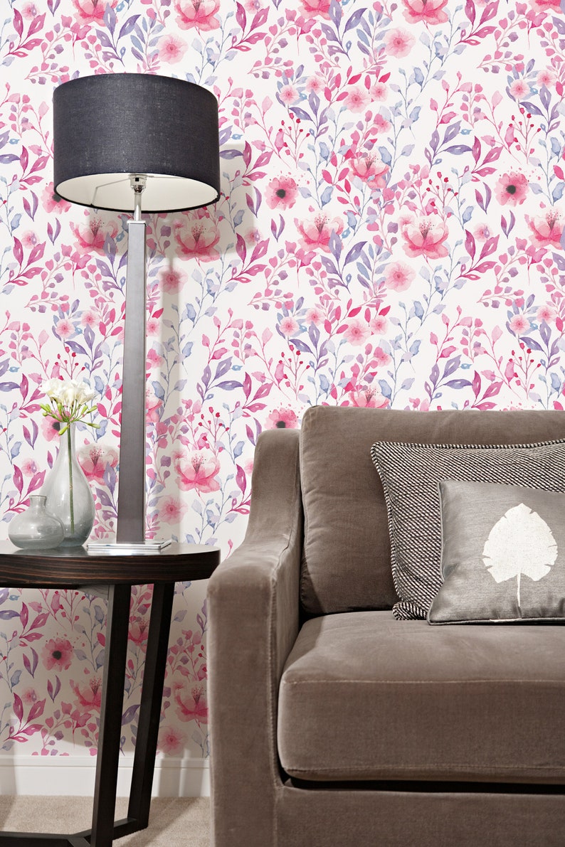 Pink Watercolor Botanical peel and stick wallpaper shows a soft floral wall design beside a gray sofa.