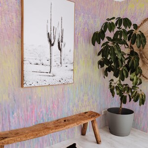 May include: A room with a black and white cactus print in a wooden frame, a wooden bench, a potted plant, and a cowhide rug. The walls are painted with a colorful abstract design in pink, yellow, and blue.