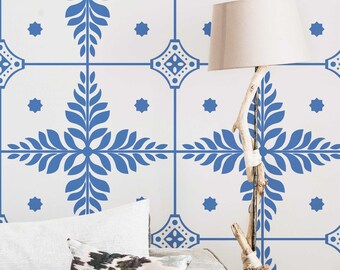 Puede incluir: Una pared blanca con un patrón de azulejos azul y blanco. El patrón de los azulejos presenta un diseño de hoja estilizado. Un sofá blanco con un cojín gris está en primer plano. Una lámpara con una pantalla blanca y una base de madera flotante está en el fondo.