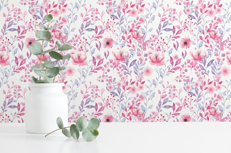 Pink Watercolor Botanical peel and stick wallpaper shows a soft floral and leafy design on a wall behind a white vase.