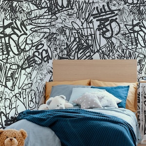 Può includere: Una camera da letto con un letto con una coperta blu navy, lenzuola azzurre e cuscini nelle tonalità del blu e dell'oro. La testiera è in legno chiaro. Il muro è coperto da graffiti neri. Un orsacchiotto e un orsacchiotto sono sul letto.