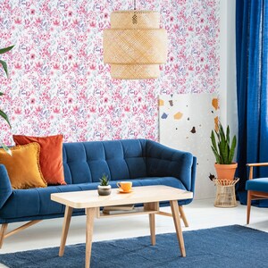 Pink Watercolor Botanical peel and stick wallpaper with a soft floral look on a living room wall behind a blue sofa.