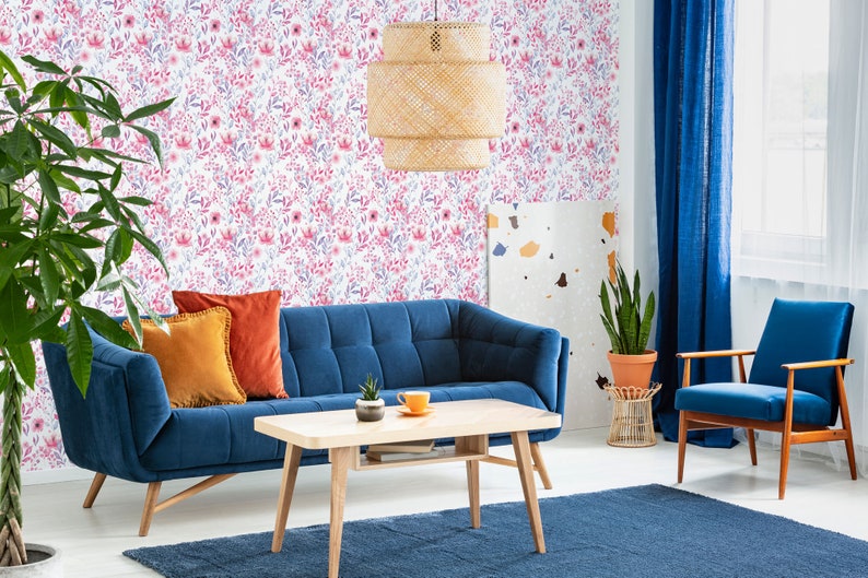 Pink Watercolor Botanical peel and stick wallpaper with a soft floral look on a living room wall behind a blue sofa.