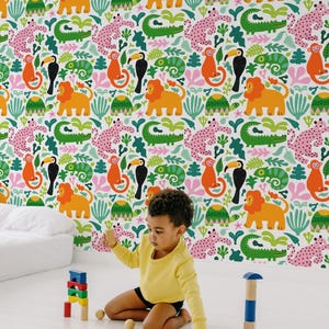 May include: A child plays with wooden blocks in front of a wallpaper featuring a colorful jungle pattern. The wallpaper design includes lions, monkeys, toucans, and other animals in a playful, cartoon style. The child wears a yellow long-sleeve shirt and black shorts.