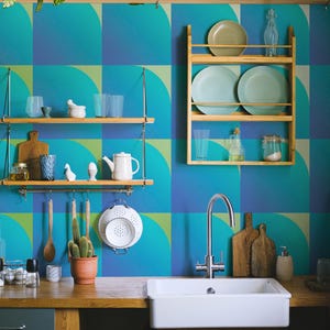 Op de afbeelding: Een keukeninterieur met een witte spoelbak, houten werkbladen en open schappen. Het blauw-groene geometrische behang vormt een levendige achtergrond. Diverse keukenartikelen, waaronder borden, glazen en keukengerei, zijn uitgestald.