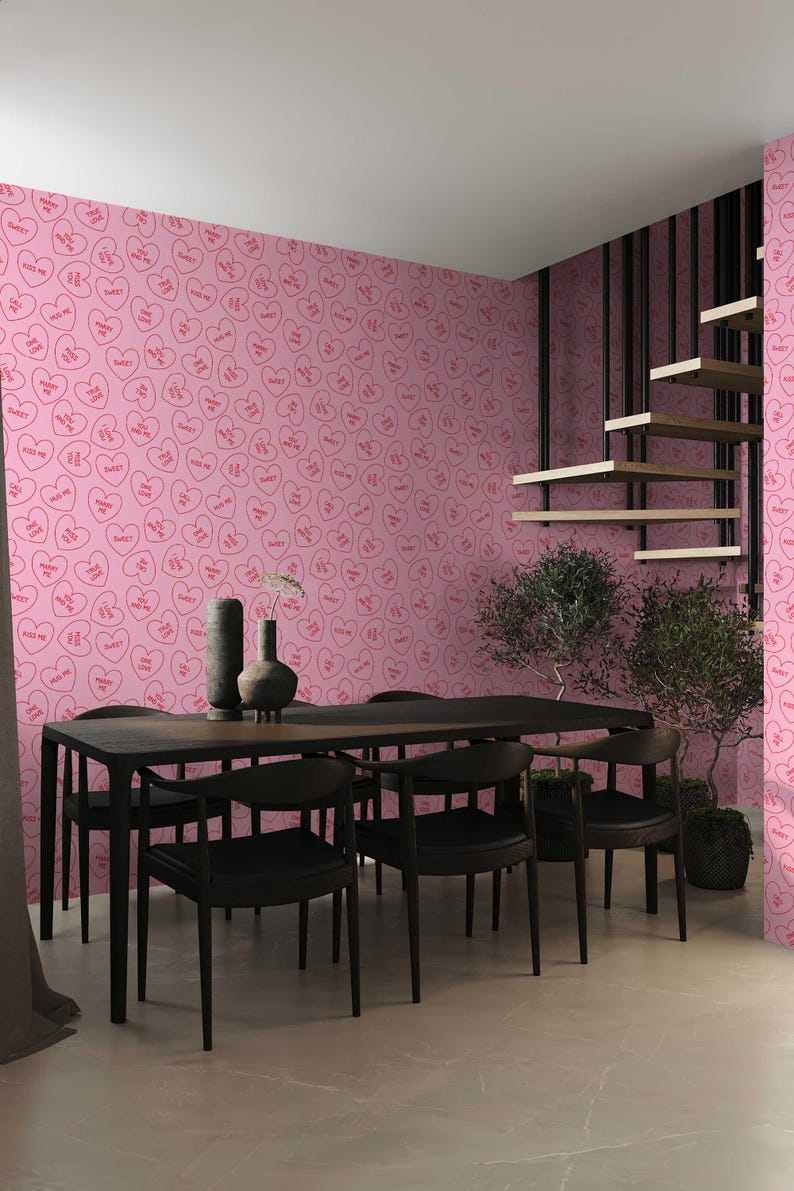 May include: A dining room with a pink wallpaper featuring a repeating pattern of red hearts with the words "Kiss Me" and "Sweet" inside. The room has a black dining table with six black chairs and a potted plant.