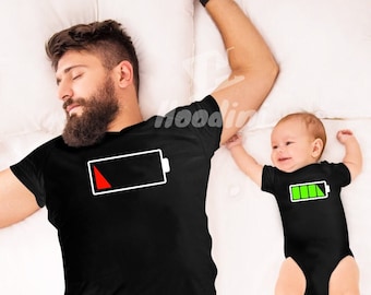May include: A father and child wearing matching black t-shirts with battery icons. The father's battery icon is red and almost empty, while the child's battery icon is green and full.
