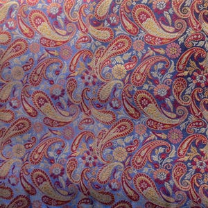 Könnte beinhalten: Nahaufnahme eines Stoffes mit Paisley-Muster in Blau-, Rot- und Goldtönen. Der Stoff hat eine strukturierte, gewebte Optik.