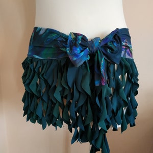 Puede incluir: Una falda de color verde azulado con volantes y un cinturón de tela estampada atado en un lazo en la parte delantera.