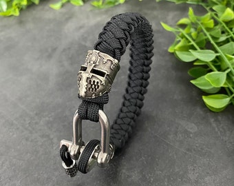 May include: A black paracord bracelet with a silver knight helmet charm and a silver clasp.