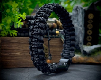 May include: A black paracord bracelet with a black metal clasp. The bracelet is made of woven paracord and has a simple design.