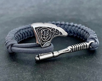 May include: A gray paracord bracelet with a silver axe charm. The axe has a Celtic knot design.