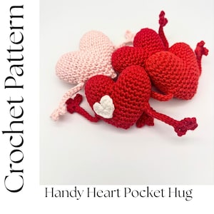 Könnte beinhalten: Häkelanleitung für einen Handy Heart Pocket Hug. Das Bild zeigt mehrere handgefertigte Häkelherzen in Rot und Rosa. Ein rotes Herz hat eine weiße Herzapplikation. Die Herzen haben Arme und Beine, was ihnen ein spielerisches Aussehen verleiht.