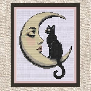May include: A cross-stitch pattern featuring a black cat sitting on a crescent moon with a human-like face. The moon is cream-colored with soft pink cheeks and lips, set against a light purple background, all enclosed within a dark brown frame.