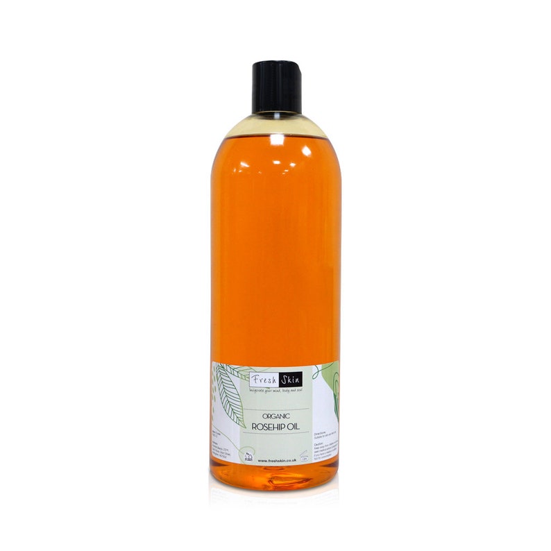 May include: A clear glass bottle with a black cap filled with orange liquid. The bottle has a label that says "Fresh Skin" and "Organic Rosehip Oil".