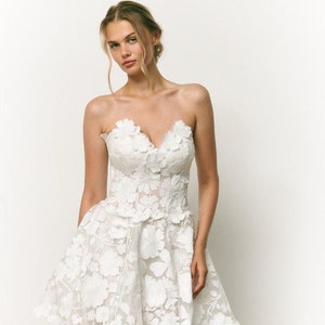 May include: A white strapless dress with a fitted bodice and a full skirt. The dress is covered in delicate floral embroidery.