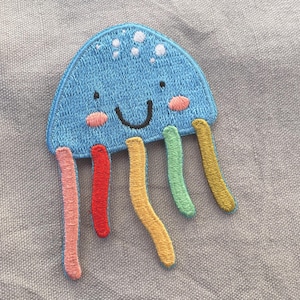 Peut inclure: Un écusson brodé bleu représentant une méduse souriante, avec des joues roses et des tentacules colorées. Le patch est un design amusant et fantaisiste, idéal pour ajouter aux vêtements ou accessoires.