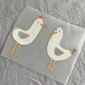 Peut inclure: Deux mouettes en papier blanc avec des becs et des pattes jaunes. Une mouette porte un chapeau rouge et l'autre un chapeau bleu. Les mouettes sont sur un fond blanc.