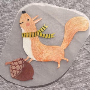 Peut inclure: Illustration fantaisiste d'un écureuil roux avec une écharpe jaune et noire et un gland marron. L'écureuil est sur un fond gris de forme irrégulière. L'œuvre a un style joyeux et de dessin animé.