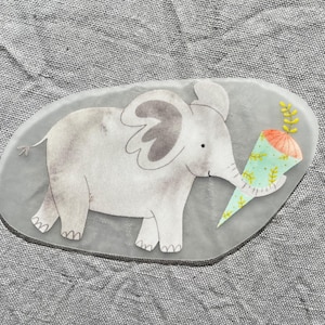 Könnte beinhalten: Ein grauer Elefant mit einem hellblauen und grünen Partyhut mit einer pfirsichfarbenen Spitze. Der Elefant hält den Partyhut in seinem Rüssel.