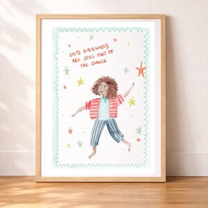 May include: A framed art print featuring a whimsical illustration of a person dancing. The person is wearing a pink striped jacket, blue striped pants, and a blue shirt. The text "Steps Backwards Are Still Part of the Dance" is written above the person, surrounded by stars.