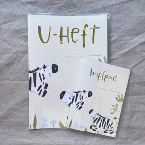 May include: A protective cover for a U-Heft and a matching Impfpass cover, both featuring a cream background with illustrations of black and white zebras, green foliage, and small blue flowers. The text U-Heft and Impfpass is printed in green.