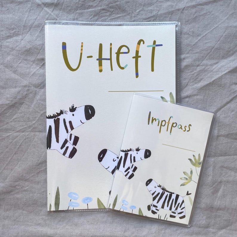 May include: A protective cover for a U-Heft and a matching Impfpass cover, both featuring a cream background with illustrations of black and white zebras, green foliage, and small blue flowers. The text U-Heft and Impfpass is printed in green.