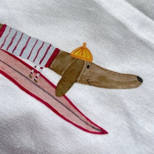 May include: A brown dachshund wearing a red and white striped shirt and a yellow hat is riding a pink surfboard.