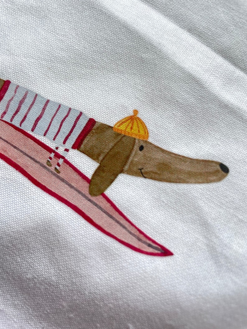 May include: A brown dachshund wearing a red and white striped shirt and a yellow hat is riding a pink surfboard.