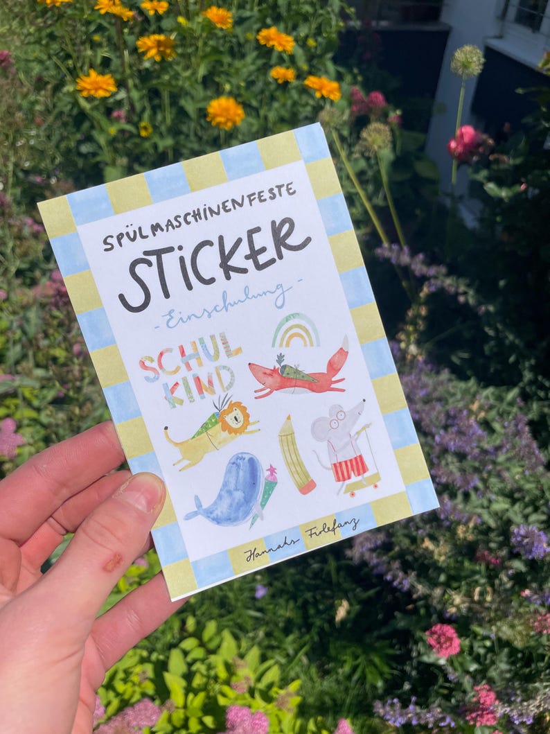 Pu&ograve; includere: Un foglio di adesivi con il testo "SP&Uuml;LMASCHINENFESTE STICKER - Einschulung - SCHUL KIND" e illustrazioni di un leone, una volpe, una balena, una matita, un topo e un arcobaleno. Il foglio ha un bordo a scacchi blu e giallo.