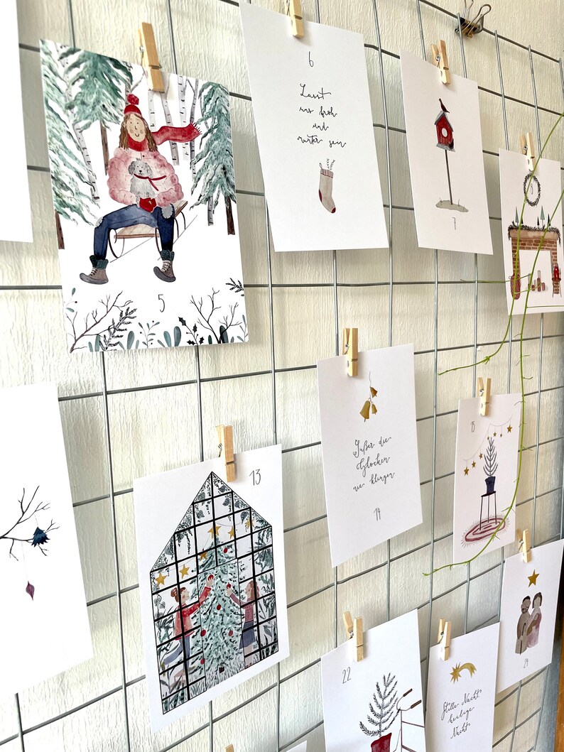 Puede incluir: Una colecci&oacute;n de tarjetas navide&ntilde;as ilustradas, sujetas a una rejilla met&aacute;lica con pinzas de madera. Las tarjetas presentan escenas invernales, decoraciones festivas y texto navide&ntilde;o. Las tarjetas est&aacute;n numeradas e incluyen im&aacute;genes de una escena de trineo, una casita para p&aacute;jaros y un &aacute;rbol de Navidad.
