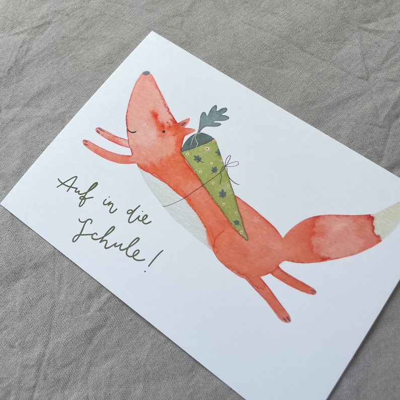 May include: A watercolour illustration of a red fox carrying a green and white cone with the text "Auf in die Schule!" on a white background.