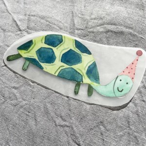May include: A green and blue watercolor illustration of a turtle wearing a pink and white polka dot party hat. The turtle has a smiling face.