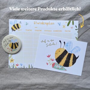 May include: A school schedule planner, a circular pin, and a rectangular card, all featuring a yellow and black bee illustration. The planner has the text "Stundenplan" and days of the week. The pin and card feature the text "Auf in die Schule!"