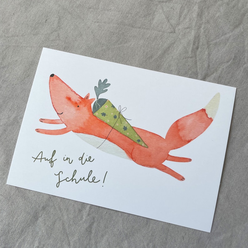 May include: A watercolour illustration of a red fox with a green and brown cone on its back. The fox is flying through the air with its tail outstretched. The text "Auf in die Schule!" is written below the fox.