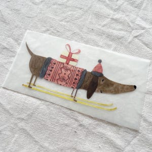 May include: A brown dachshund wearing a red and white sweater and a red hat is skiing with a yellow and white gift box on its back.