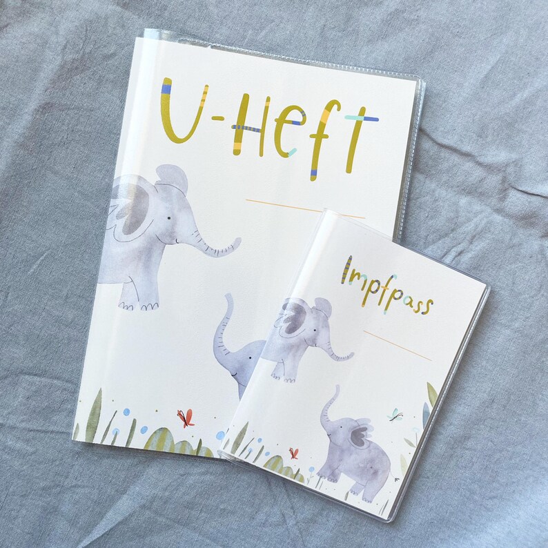 May include: Two clear plastic covered folders with a white background and colourful elephant illustrations. The larger folder has the text "U-Heft" in yellow. The smaller folder has the text "Impfpass" in black.