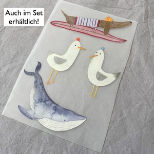 May include: A set of four illustrated stickers featuring a blue whale, two seagulls, and a dachshund riding a surfboard. The text "Auch im Set erh&auml;ltlich!" is printed on the sheet.