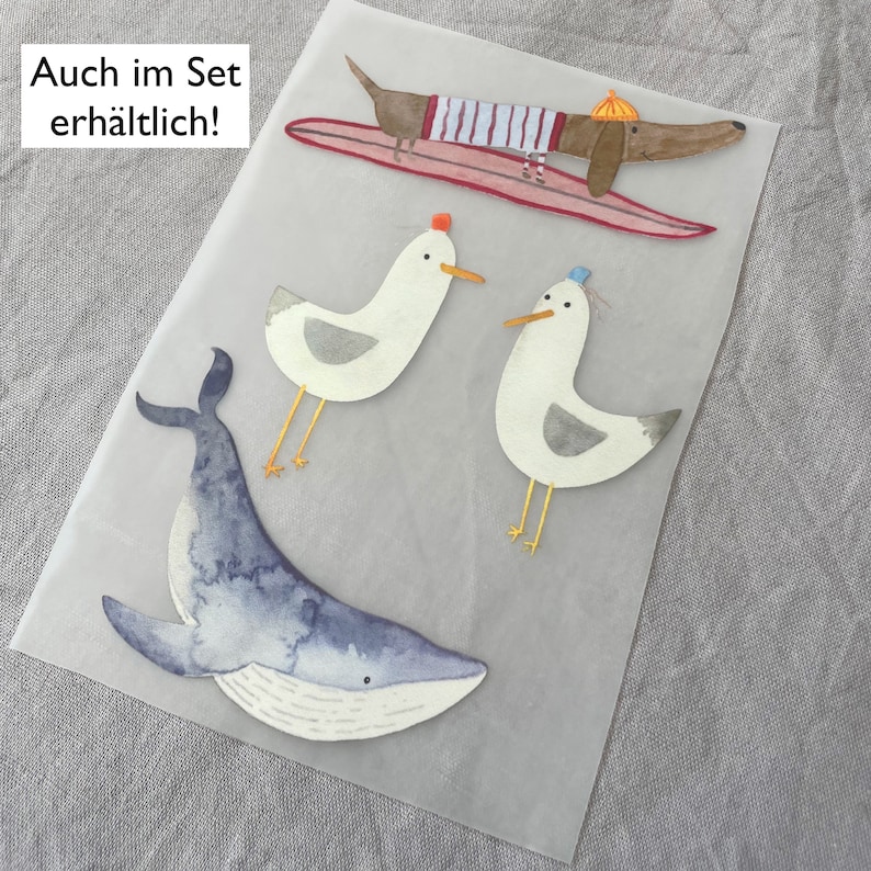 May include: A set of four illustrated stickers featuring a blue whale, two seagulls, and a dachshund riding a surfboard. The text "Auch im Set erh&auml;ltlich!" is printed on the sheet.