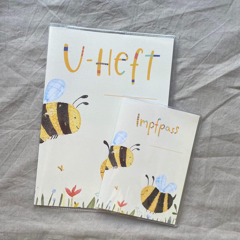 May include: Two rectangular protective covers for documents, featuring a cream background with illustrations of yellow and black striped bees, blue wings, and small colorful flowers. The larger cover displays the text U-Heft, and the smaller cover displays the text Impfpass in a colorful, playful font.