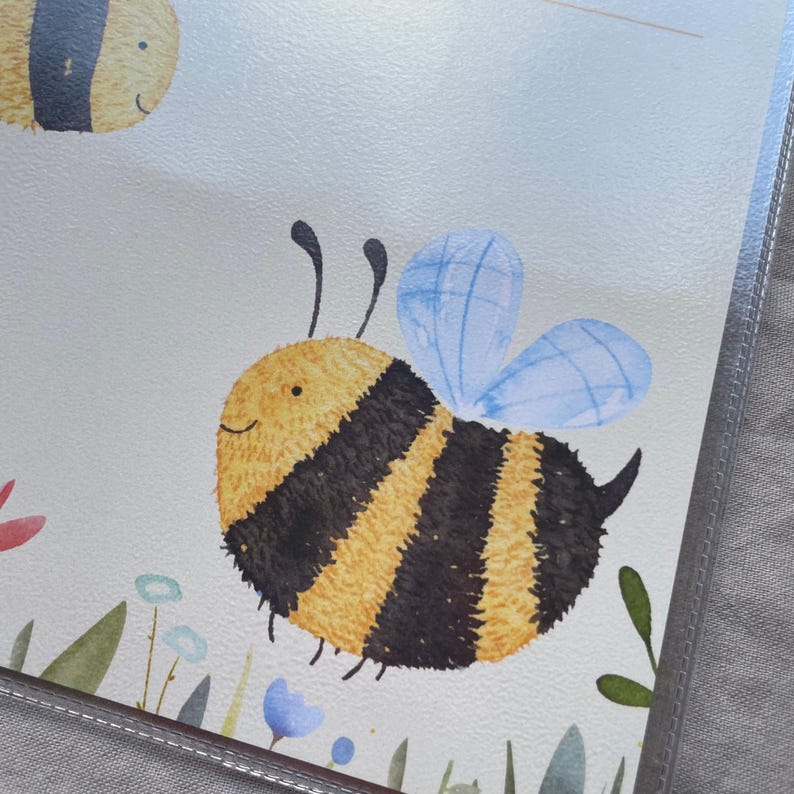 May include: A watercolor illustration on a light background featuring a round, fuzzy bee with yellow and black stripes, two antennae, and light blue wings. Below the bee are small, simple watercolor depictions of green leaves and blue flowers.