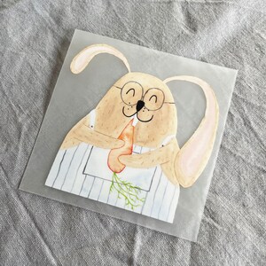 May include: A watercolor illustration of a brown bunny wearing glasses and a blue and white striped apron, holding a carrot in its paws.