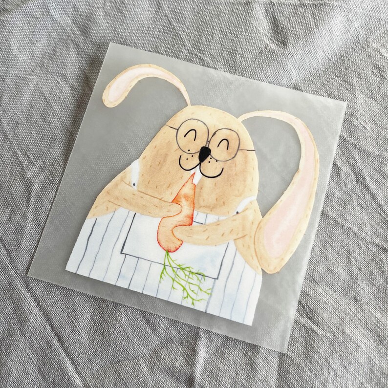 May include: A watercolor illustration of a brown bunny wearing glasses and a blue and white striped apron, holding a carrot in its paws.