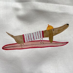 May include: A brown and white dachshund wearing a striped shirt and a yellow hat is surfing on a pink surfboard.