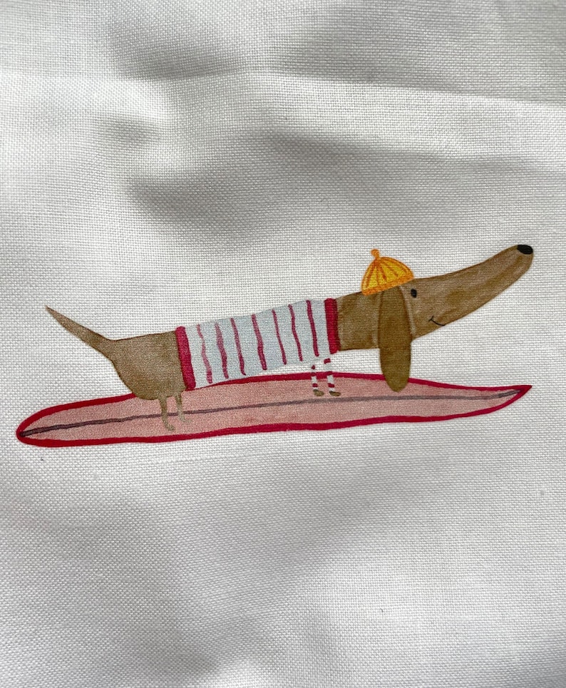 May include: A brown and white dachshund wearing a striped shirt and a yellow hat is surfing on a pink surfboard.