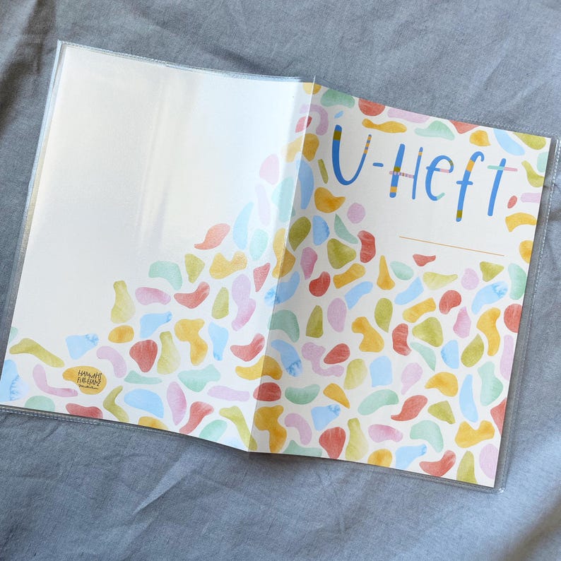 May include: A white notebook with a clear plastic cover. The cover has a colorful abstract design with a title that reads "U-Heft".