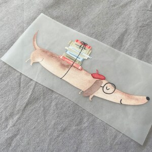 May include: A brown dachshund with a red beret and round glasses carries a stack of books tied with a red ribbon.