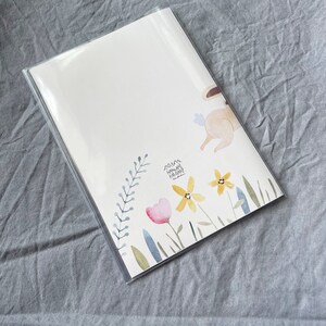 May include: A white card with a watercolor illustration of a bunny rabbit hopping over a field of flowers. The flowers are yellow, pink, and blue. The text "Mama Happy Birthday" is written on the card.